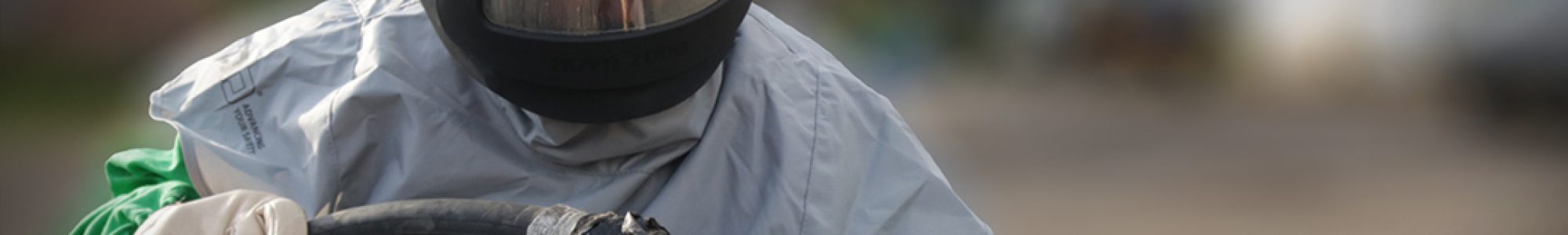 Contractor in protective helmet and clothing holding a shot blasting gun in use.
